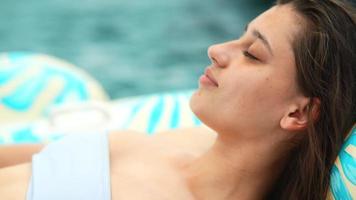 Close up of a beautiful young woman in black and white bikini  lounges on a flamingo float in a pool video