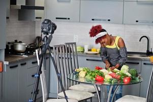 mujer afroamericana filmando la transmisión de su blog sobre comida saludable en la cocina de casa. ella corta el repollo. foto