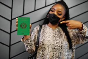 mujer africana con mascarilla negra muestra el pasaporte de guinea en la mano. coronavirus en el país africano, cierre de fronteras y cuarentena, concepto de brote de virus. foto