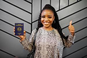 Close up portrait of young positive african american woman holding Paraguay passport and thumbs up. photo