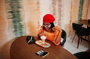 Elegant afro american woman in red french beret, big gold neck chain polka dot blouse pose indoor. photo