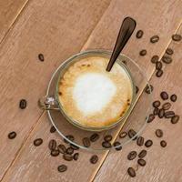 vista superior de una taza de café con leche caliente o capuchino en una taza de vidrio sobre una mesa de madera. café con espuma de leche con espacio de copia foto
