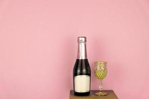 champagne bottle and glass wine with golden glitter on pink background. Mockup with copy space photo