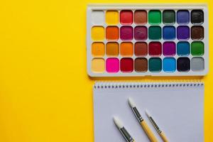 Watercolor paints and brushes on yellow background, top view. Creative artistic mockup with copyspace. Aquarelle painting photo