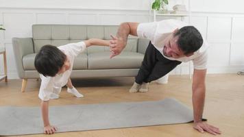 el padre y el hijo tailandeses asiáticos son ejercicios de entrenamiento físico y practican yoga en el piso de la sala de estar, bromean juntos por la salud y el bienestar, feliz estilo de vida doméstico en el fin de semana familiar. video