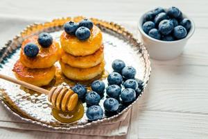 Homemade cheesecake with freshly picked juicy blueberries in the plate on wooden background, close up photo