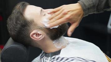 le coiffeur applique de la crème à raser sur le visage du cou du client masculin video