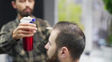 el peluquero usa una botella de spray para rociar el cabello del cliente masculino antes de peinarlo video