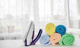 Towels folded in a roll and an iron after ironing on an ironing board. housekeeping concept photo