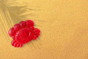 Red plastic shrimp on sand beach background, close-up. Childrens toys for bathing babies. Educational games for children, preschool education. Layout, preparation of toys for the designer or website. photo