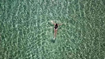 Aerial zoom out of a woman diving and swimming in crystal clear water