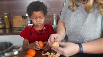 Young girl and adult woman peel oranges together in a kitchen video