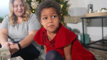 Young girl in red dress talks and sits next to adult woman in front of a decorated Christmas tree video