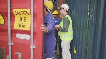 Group of multiracial workers in safety uniforms and hardhats walk and inspect shipping cargo with White male manager at nook of container stack, import and export goods logistic transport industry. video