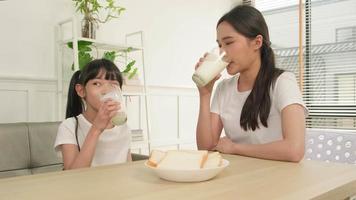 A Healthy Asian Thai family, little daughter, and young mother drink fresh white milk in glass and bread joy together at a dining table in morning, wellness nutrition home breakfast meal lifestyle. video