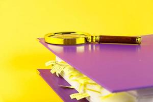 Documents with sticky bookmarks in an office folder and a magnifying glass on a yellow background. Copy space. photo