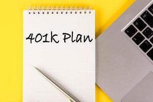 Paper with a 401k plan on the table with a laptop on a yellow background. photo