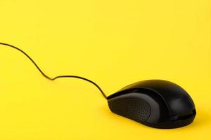 Black mouse with a cord on a yellow background. Empty place for text. photo