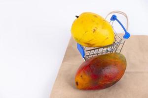 Various types of mangoes with yellow and red peels, a favorite Thai fruit in a shopping cart, and a paper bag, on a white background. ECO, environmentally friendly product. Copy space. photo