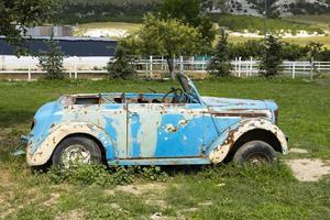 un viejo coche azul oxidado enraizado en el suelo. foto