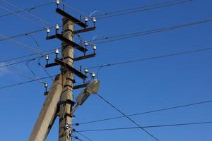 un poste eléctrico con cables y una lámpara de alumbrado público contra el cielo azul durante el día. foto