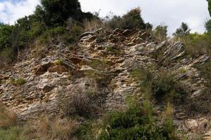 Rocky cliff with cracks and ledges with lush vegetation at the top. Shale texture in Dinaric Alps, Montenegro photo