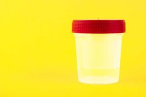 Empty, transparent plastic, white container with a red lid for collecting urine on a yellow background. Copy space. photo