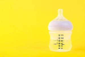 Baby bottle for milk with water and a pacifier on a yellow background. Copy space. photo