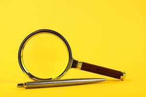 A magnifying glass in a gold frame and a pen on a yellow background. Copy space. photo