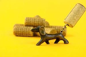 Close-up of a group of antique dated wine corks and an old corkscrew, in the form of a dachshund dog. On a yellow background. Copy space. photo