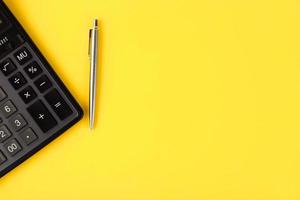 A flat lay or top view of a gray pen with a calculator on a bright yellow background with blank copy space, math calculation, cost, tax or investment. photo