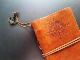 A notebook with a brown leather cover with a compass motif and anchor strap. photo