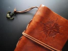 A notebook with a brown leather cover with a compass motif and anchor strap. photo