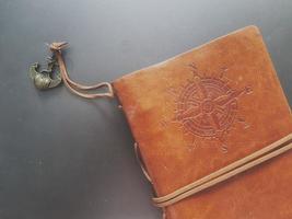 A notebook with a brown leather cover with a compass motif and anchor strap. photo