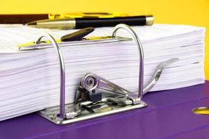 Close up of a pile of unfinished documents awaiting verification, a magnifying glass, on a yellow background. Business and education concept. Copy space photo