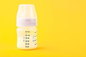 White plastic baby bottle with pacifier, rich in baby food, on yellow background. Copy space. photo