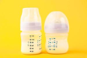 White plastic baby bottle with pacifier, rich in baby food, on yellow background. Copy space. photo