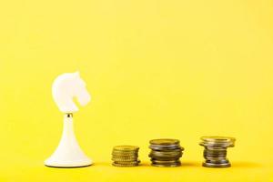 White chess piece of a horse, with coins in the form of steps on a yellow background. Business concept. Game, strategy, wisdom, determination. Copy space. photo