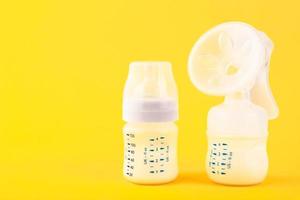 White plastic baby bottle with pacifier,breast pump rich in baby food, on yellow background. Copy space. photo