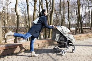 día de la Madre. mujer joven caminando en el parque de primavera con carro de bebé. madre pasa tiempo con su hijo al aire libre foto
