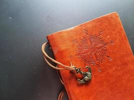 A notebook with a brown leather cover with a compass motif and anchor strap. photo