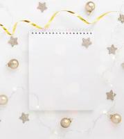 White sheet of notebook on white table with stars, Christmas balls and festive garland. Concept planning, wish list for the new year. photo