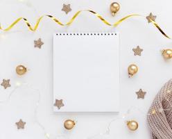 White sheet of notebook on white table with stars, Christmas balls and festive garland. Concept planning, wish list for the new year photo