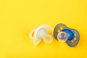 Baby pacifiers in different colors. yellow background. Copy space. Selective focus. photo