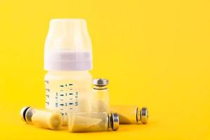 botella de plástico blanco con chupete, burbujas, ampollas con probiótico seco, bifidobacterias en el interior sobre un fondo amarillo. copie el espacio foto