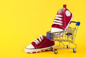 un par de zapatillas rojas en un carro sobre un fondo amarillo. las compras en línea. comercio electrónico. copie el espacio foto