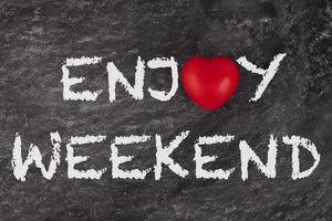 Enjoy weekend. The text is written on a school board with a white piece of chalk with a red heart. concept photo