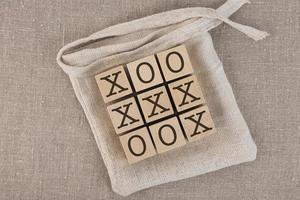 Bloques de madera de tres en raya con bolsa. jugar sobre un fondo de lino gris, también conocido como tic-tac-toe. foto