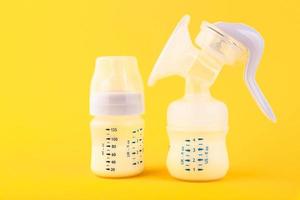 White plastic baby bottle with pacifier,breast pump rich in baby food, on yellow background. Copy space. photo