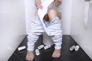 Woman pissing, with diarrhea on a white toilet bowl in the toilet with a roll of paper in her hand. photo